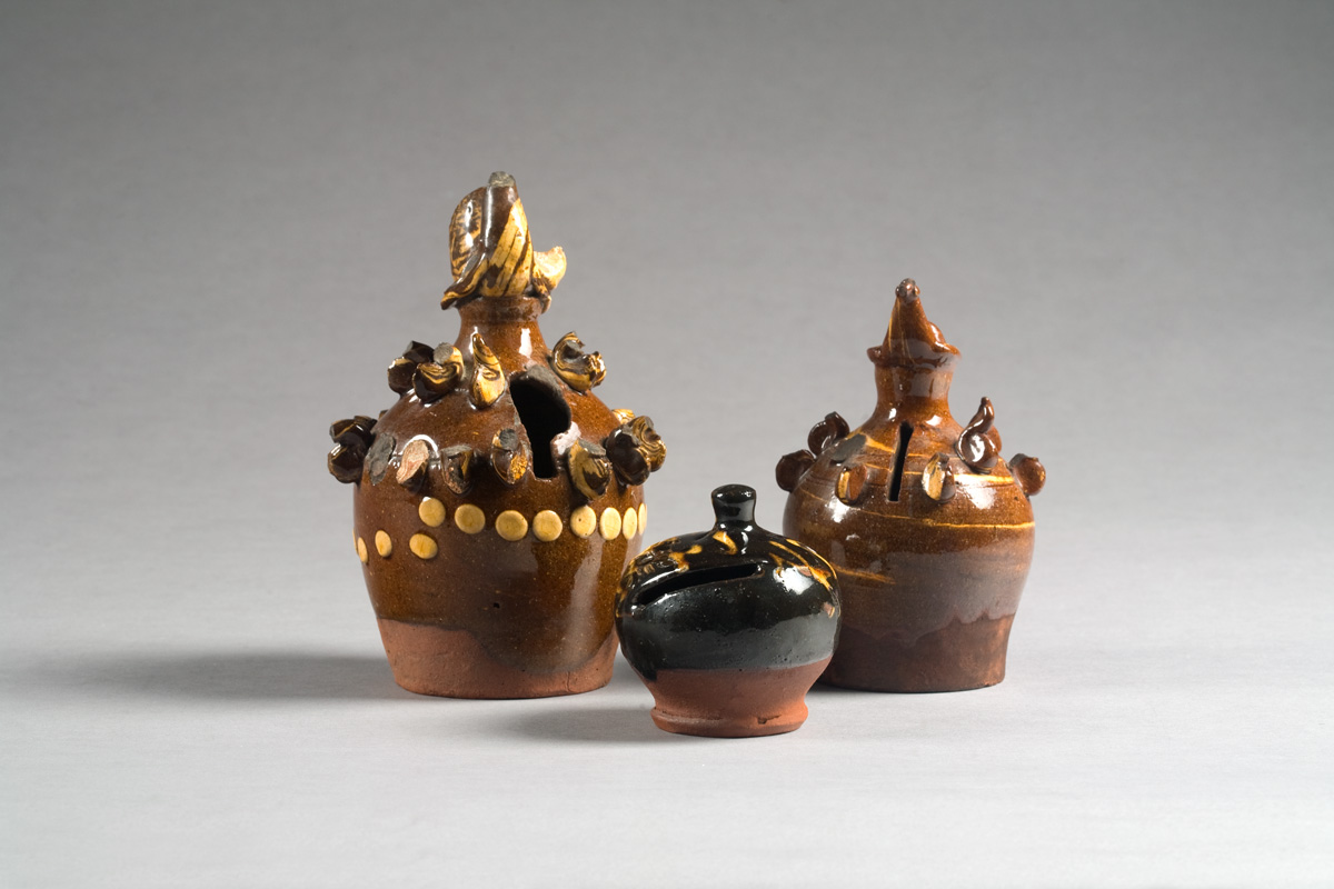 Appraisal: THREE GLAZED REDWARE BANKS The first two surmounted by the