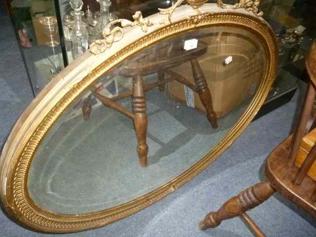 Appraisal: AN OVAL GILT FRAMED WALL MIRROR with bevelled glass and