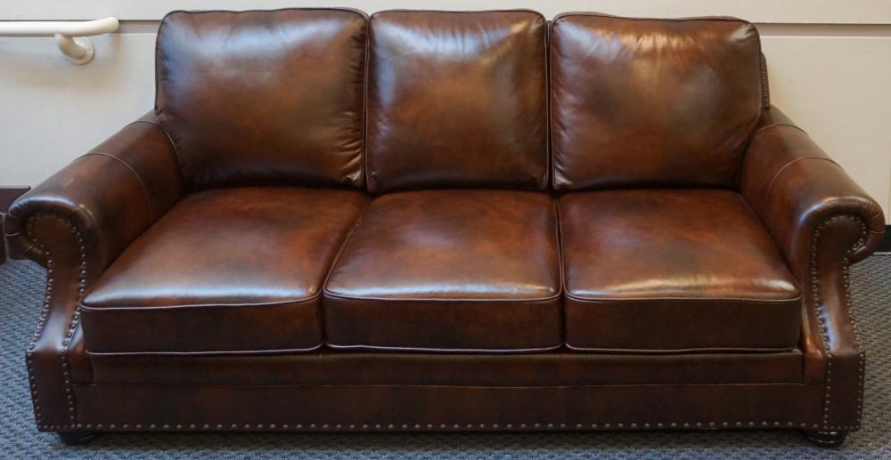 Appraisal: ABBYSON LIVING BROWN LEATHER AND NAIL STUDDED THREE-CUSHION SOFA APPROX