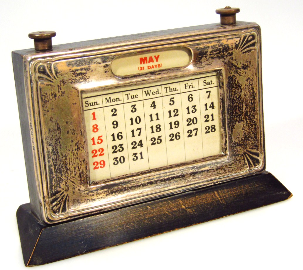 Appraisal: A George V silver and ebonised desk calendar the shaped