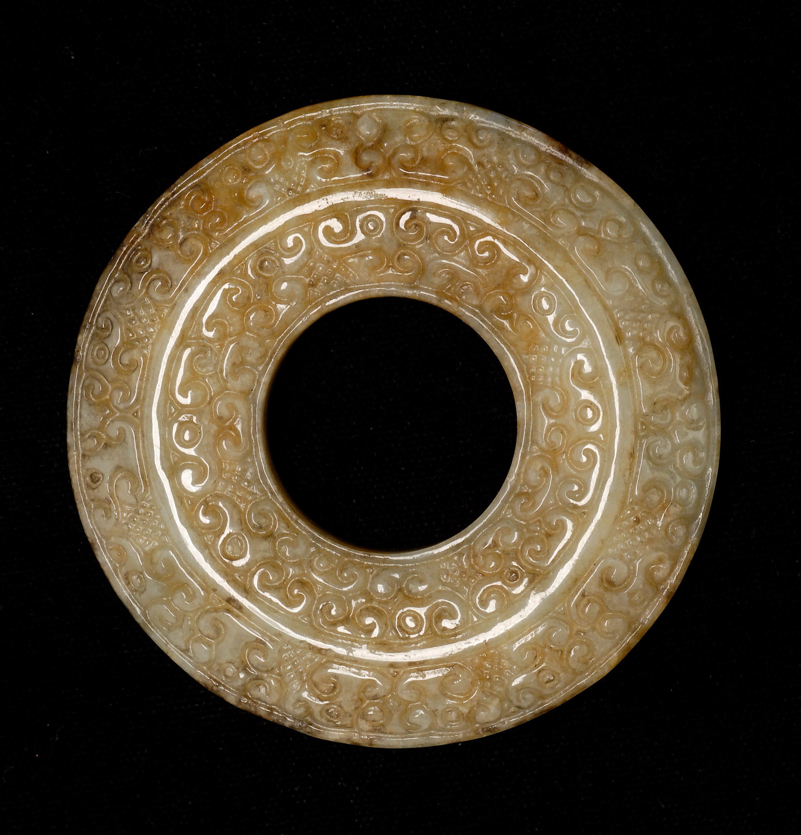 Appraisal: CELADON AND BROWN JADE BI With stylized dragon carving Diameter