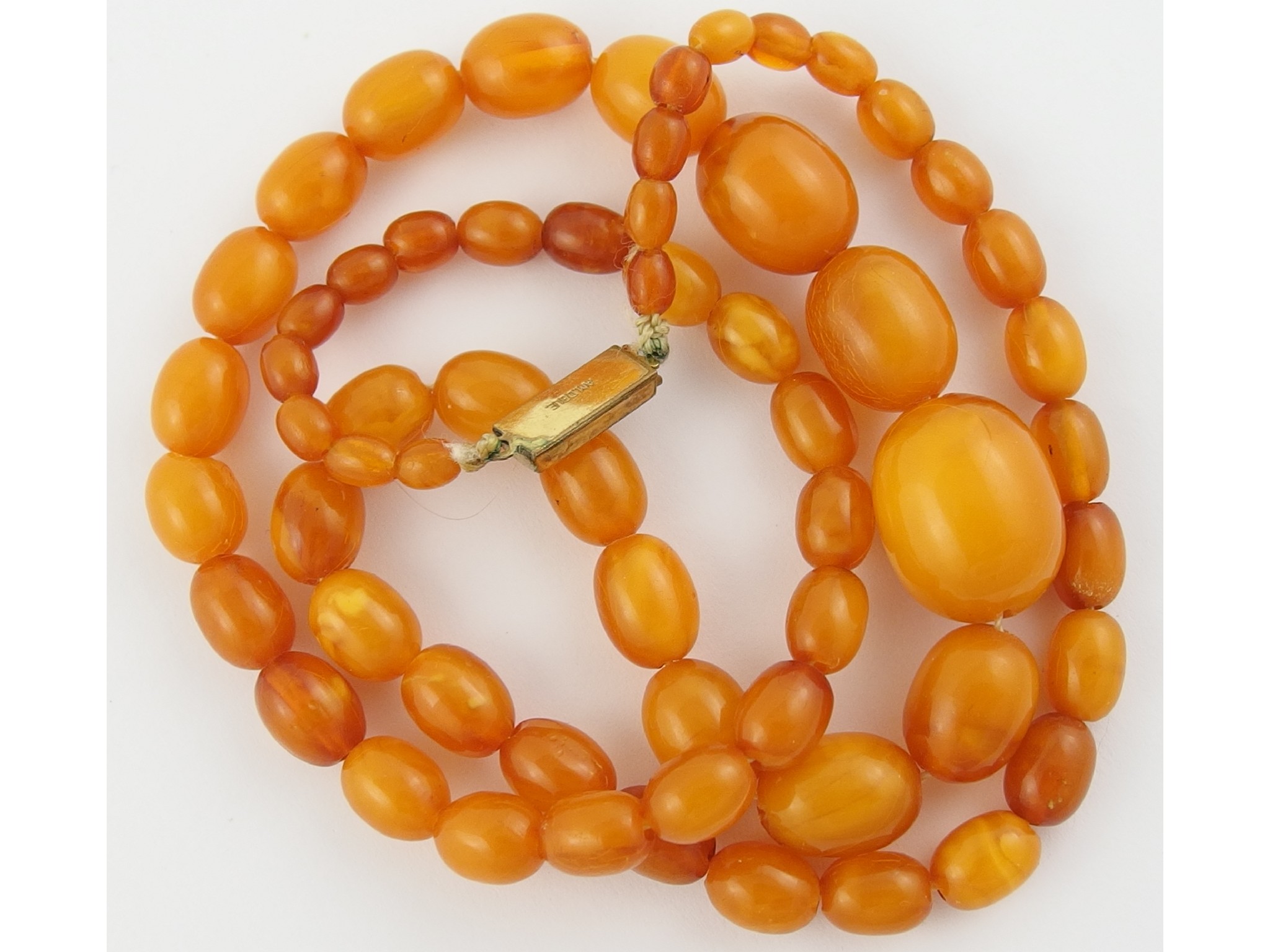 Appraisal: A string of orange amber coloured beadsbeads range in size