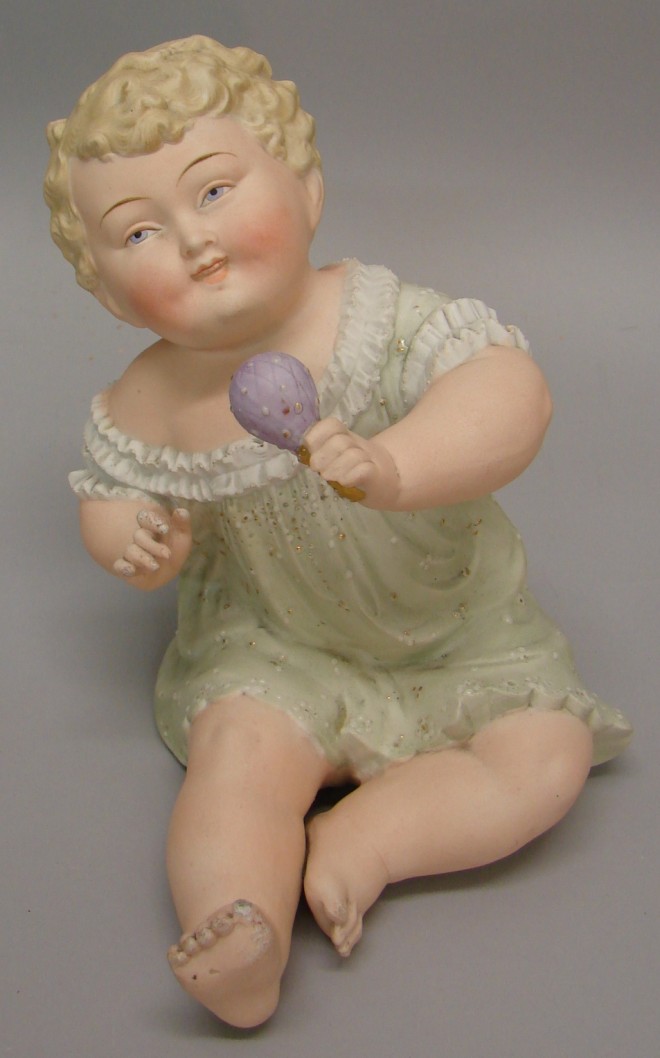 Appraisal: Unmarked sitting bisque baby holding a lavender rattle Child is