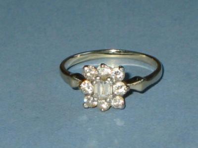 Appraisal: A DIAMOND CLUSTER RING with emerald cut centre set within