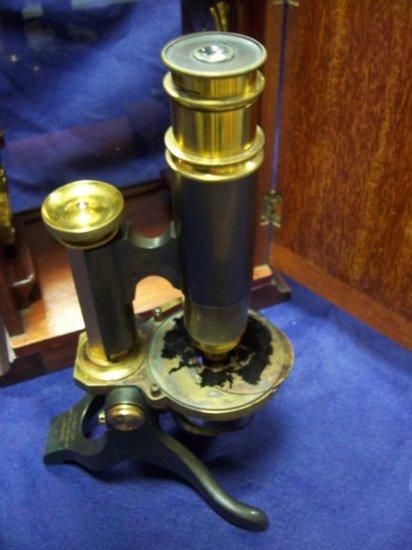 Appraisal: An ebonised metal and brass mounted microscope with fitted magnifying