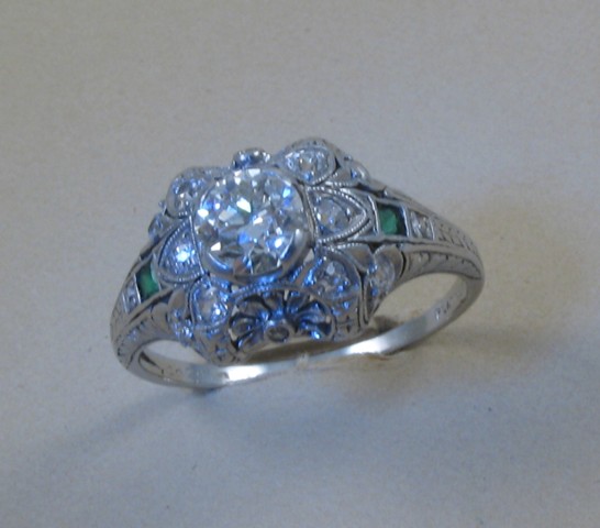 Appraisal: ESTATE EMERALD DIAMOND AND PLATINUM RING centering a round-cut diamond