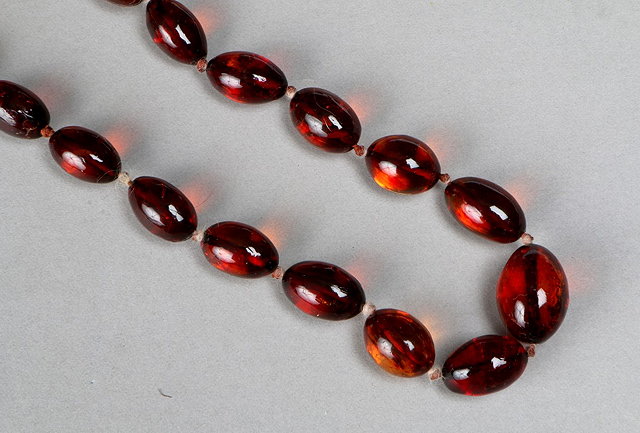 Appraisal: A CLEAR CLARET COLOURED OVAL AMBER BEAD NECKLACE largest bead