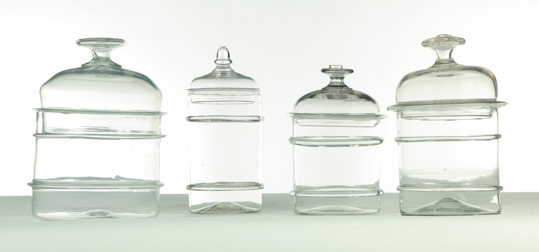 Appraisal: FOUR BLOWN CLEAR GLASS STORAGE JARS WITH LIDS American mid