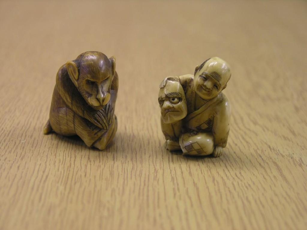 Appraisal: Two Japanese carved ivory netsuke man seated holding mask monkey