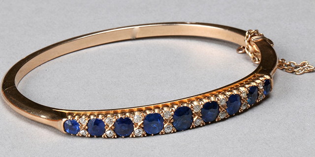 Appraisal: AN EDWARDIAN SAPPHIRE AND DIAMOND SET HINGED BANGLE nine oval