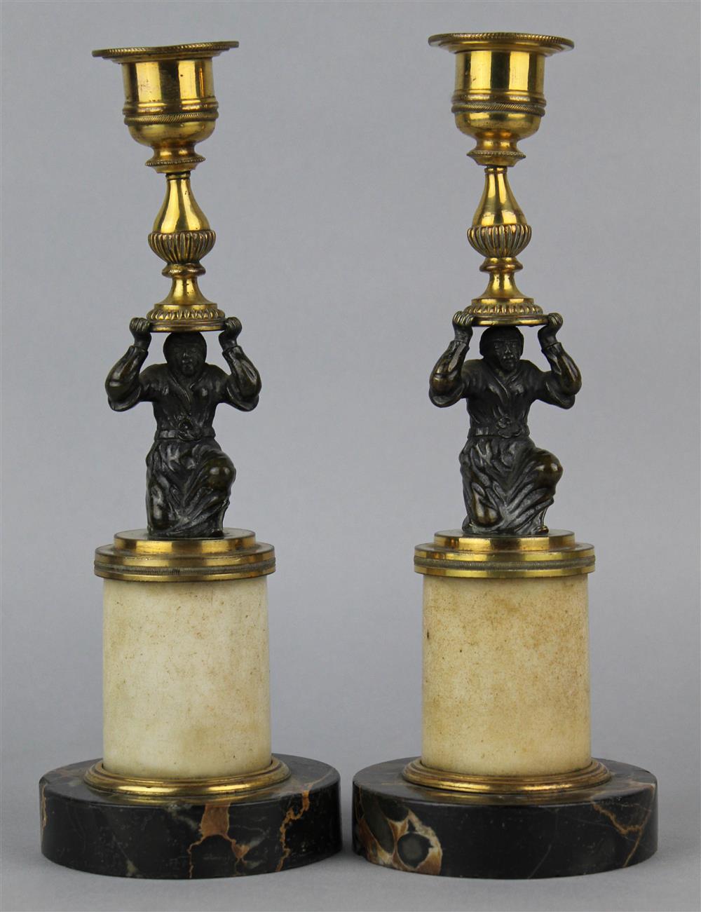 Appraisal: PAIR OF BRASS AND MARBLE FIGURAL CANDLESTICKS the plain cylindrical