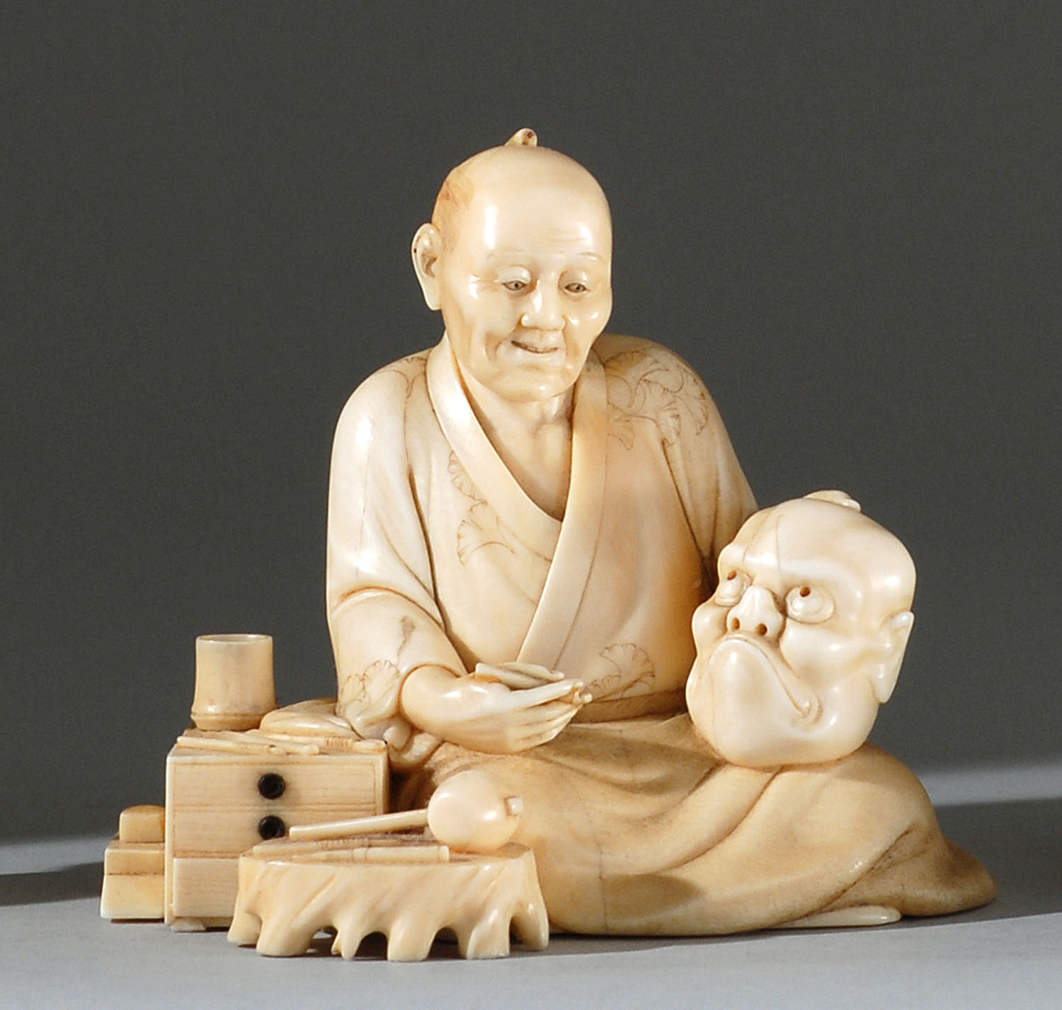 Appraisal: IVORY OKIMONO Meiji PeriodDepicting a mask carver holding a comic