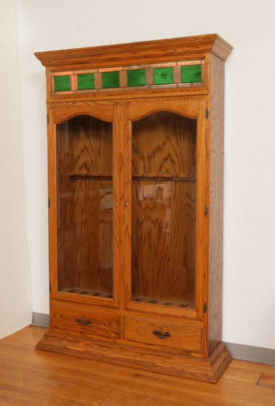 Appraisal: OAK STAINED GLASS GUN CABINET Shaped pediment over panels of