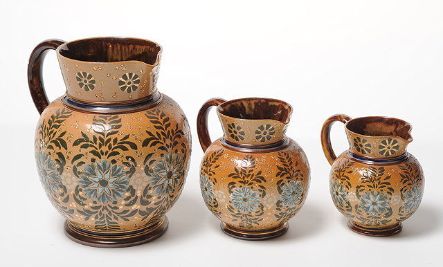 Appraisal: A GRADUATED SET OF THREE LAMBETH DOULTON GLAZED POTTERY JUGS