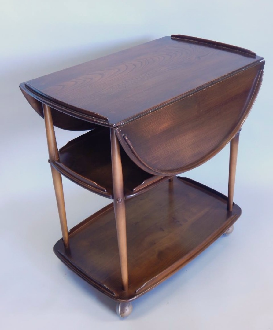 Appraisal: An Ercol mid coloured elm drop leaf trolley on turned