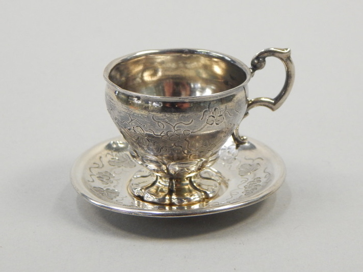 Appraisal: A Continental miniature white metal cup and saucer engraved with