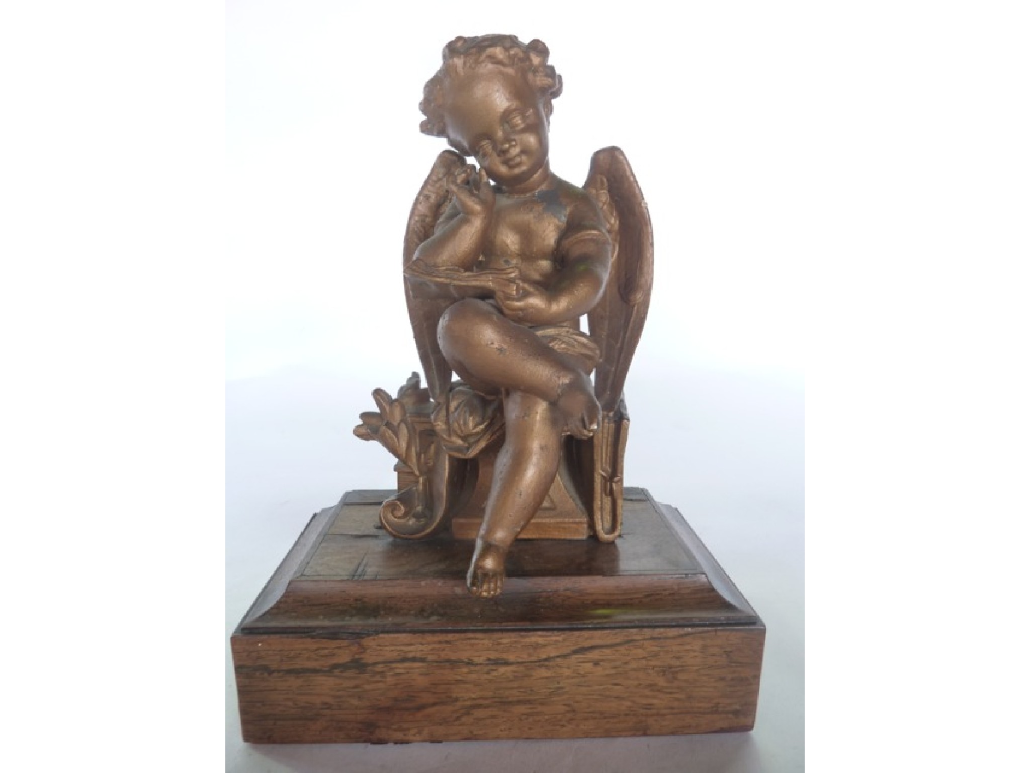 Appraisal: A painted spelter figure of a seated winged cherub cross