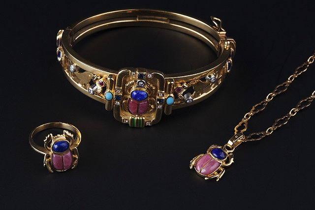 Appraisal: AN EGYPTIAN REVIVAL VARI GEM-SET AND ENAMEL SUITE comprising a