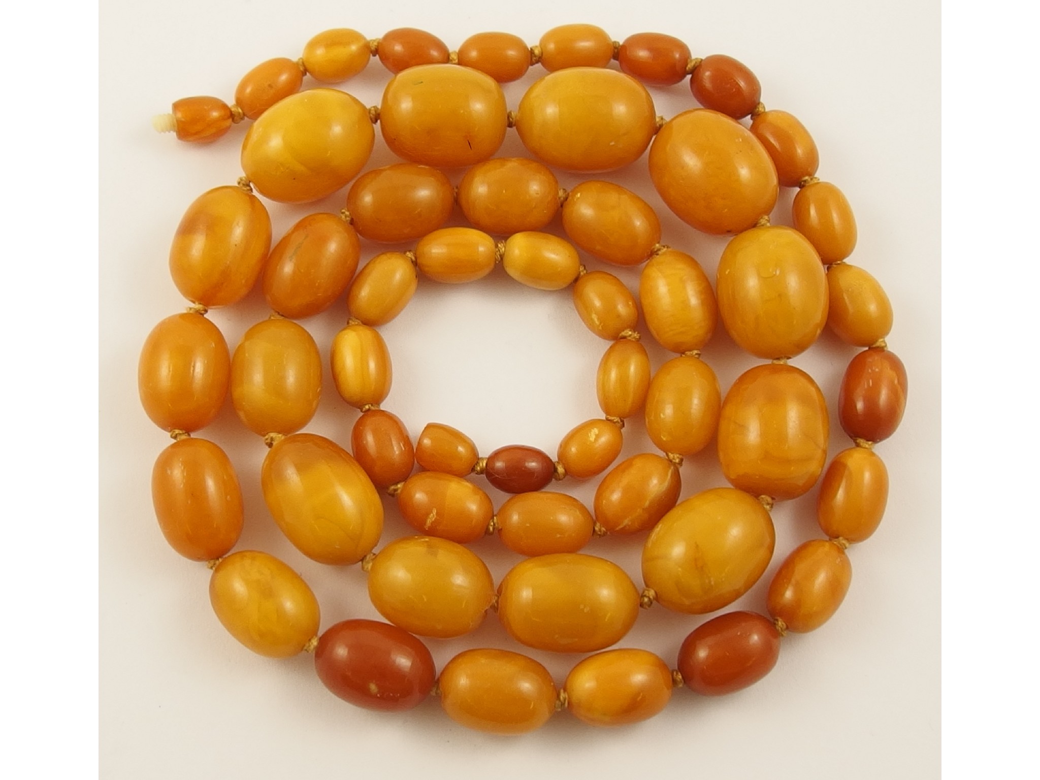 Appraisal: A string of butterscotch amber coloured beadsmainly opaque with translucent