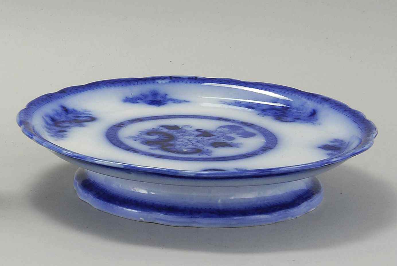 Appraisal: RARE FLOW BLUE FOOTED CAKE PLATEMid- th CenturyIn the Hong