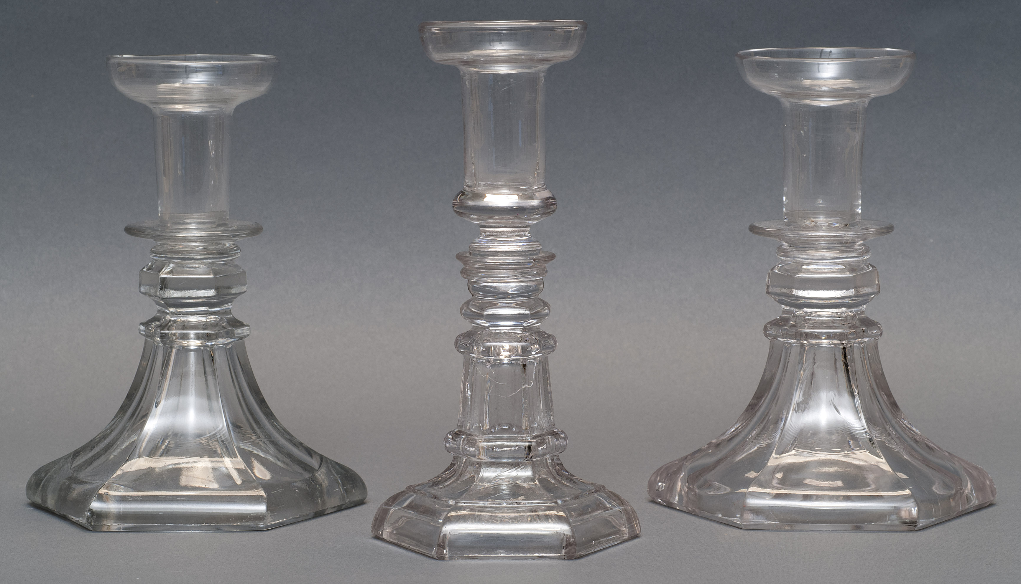 Appraisal: THREE SANDWICH GLASS COMPANY CLEAR GLASS CANDLESTICKS Second Quarter of