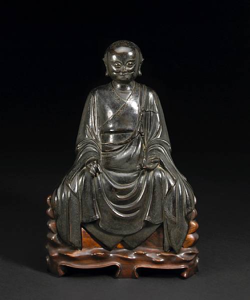 Appraisal: A bronze seated luohan Ming Dynasty The sharply featured priest