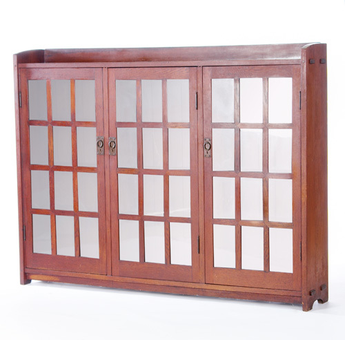 Appraisal: GUSTAV STICKLEY Triple-door mitered-mullion bookcase with twelve panes per door