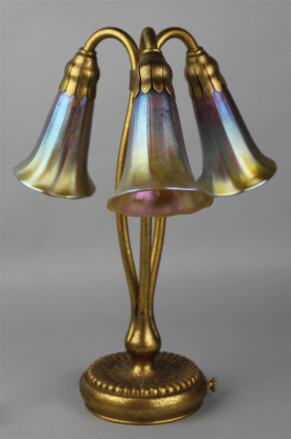 Appraisal: TIFFANY STUDIOS GILT BRONZE AND FAVRILE GLASS THREE-LIGHT 'LILY' TABLE