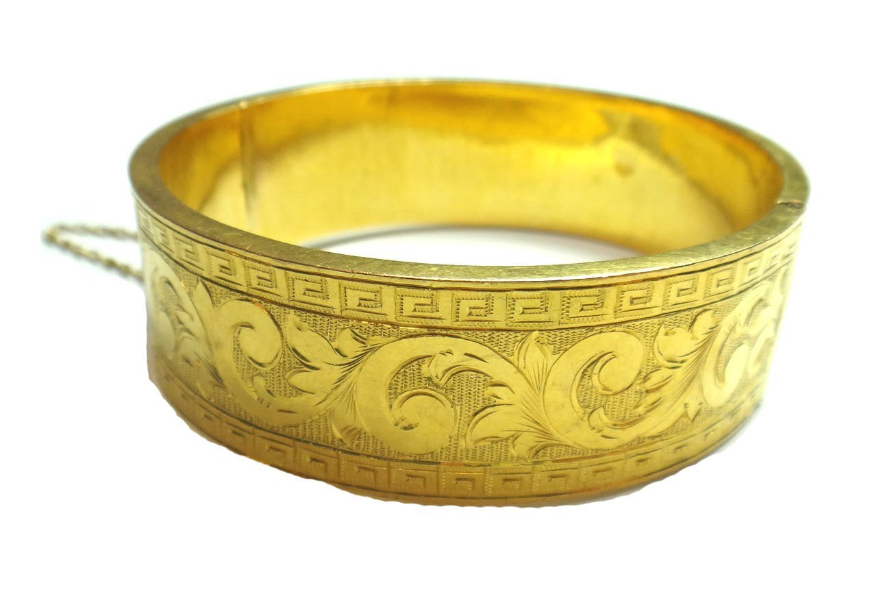 Appraisal: A gold circular hinged bangle with foliate scroll engraved decoration