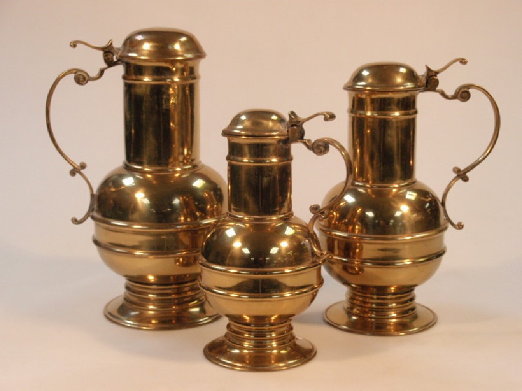 Appraisal: Three graduated brass flagons with scroll handles thC style