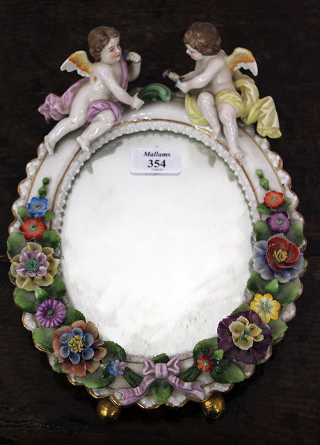 Appraisal: A CONTINENTAL PORCELAIN OVAL MIRROR crested with two cherubs floral