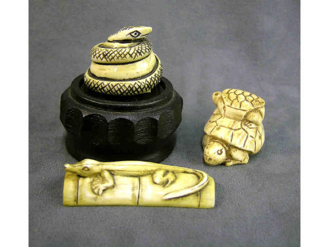 Appraisal: Three lightly stained ivory netsuke including coiled snake with stand