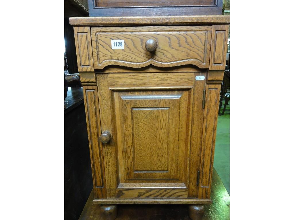 Appraisal: An oak bedside cupboard enclosed by a panelled door beneath