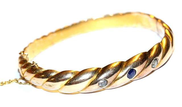 Appraisal: A GOLD HINGED BANGLE of hollow twisted form set with