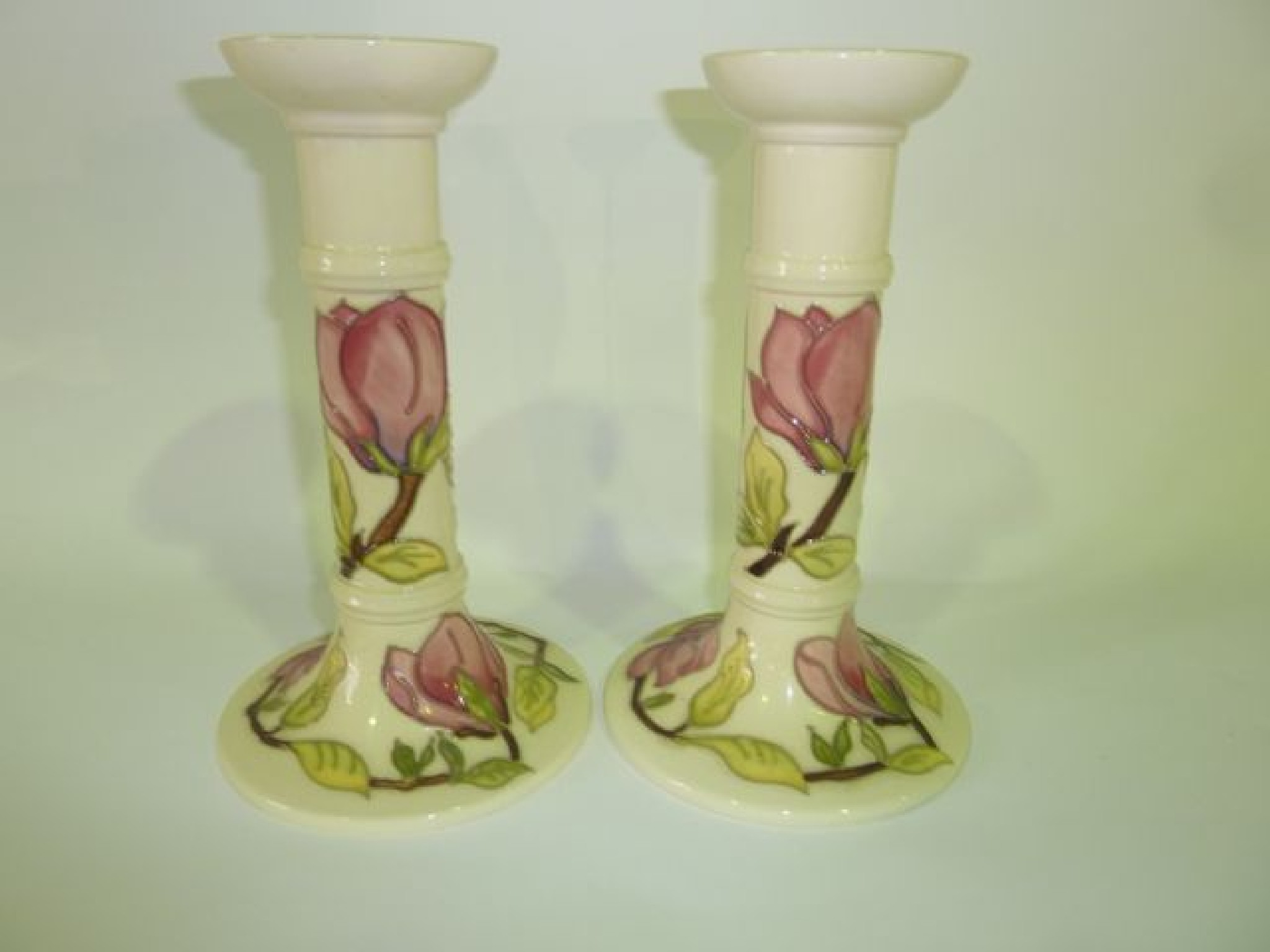 Appraisal: A pair of Moorcroft cream ground candlesticks in the Magnolia