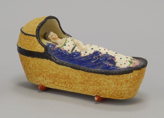 Appraisal: PEARLWARE ENAMEL CRADLE WITH SLEEPING CHILD Early th CenturyBasketweave hooded