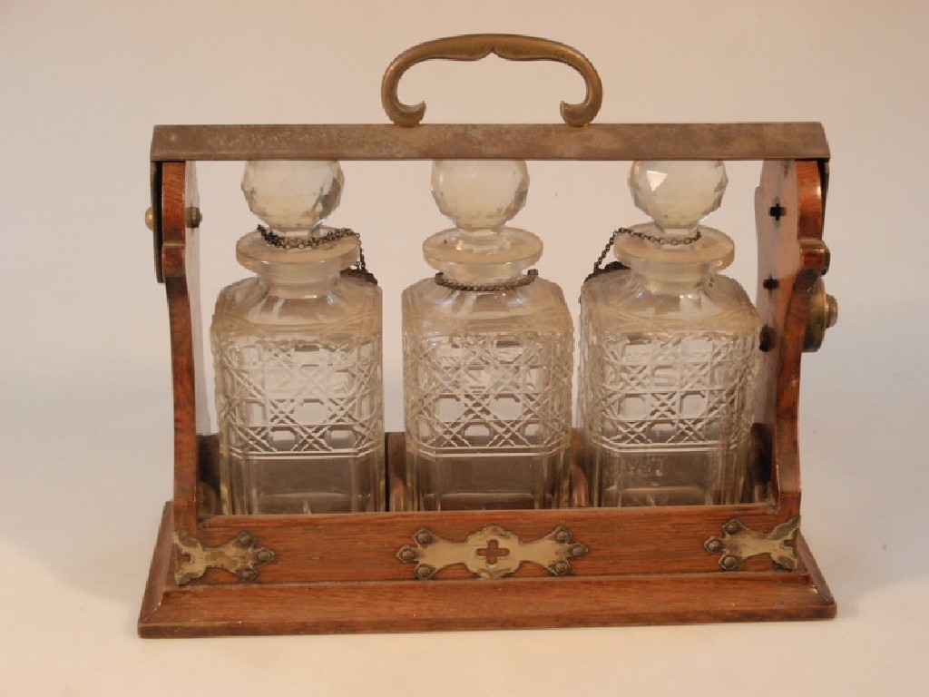 Appraisal: An oak three bottle Tantalus with cut glass decanters hung