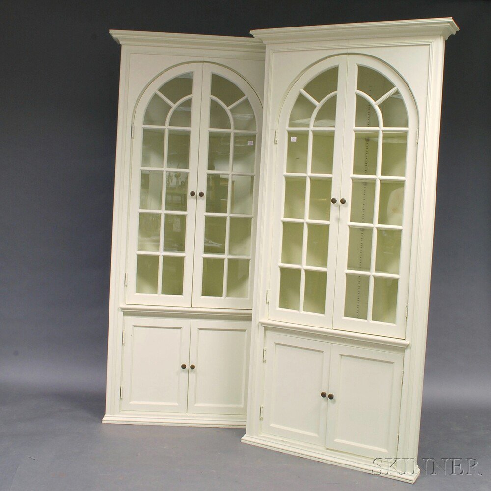 Appraisal: Pair of White-painted Glazed Corner Cupboards the arched doors revealing