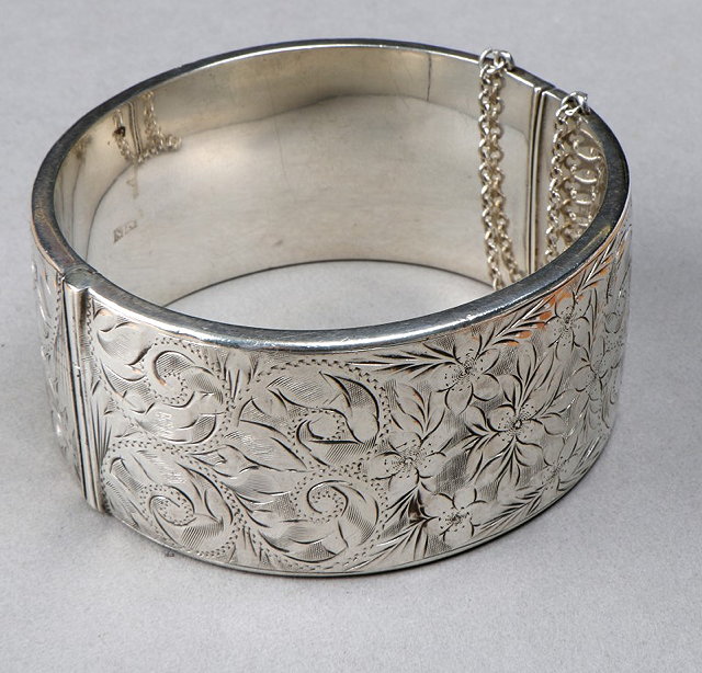 Appraisal: A SILVER HOLLOW HINGED BANGLE with engraved foliate decoration