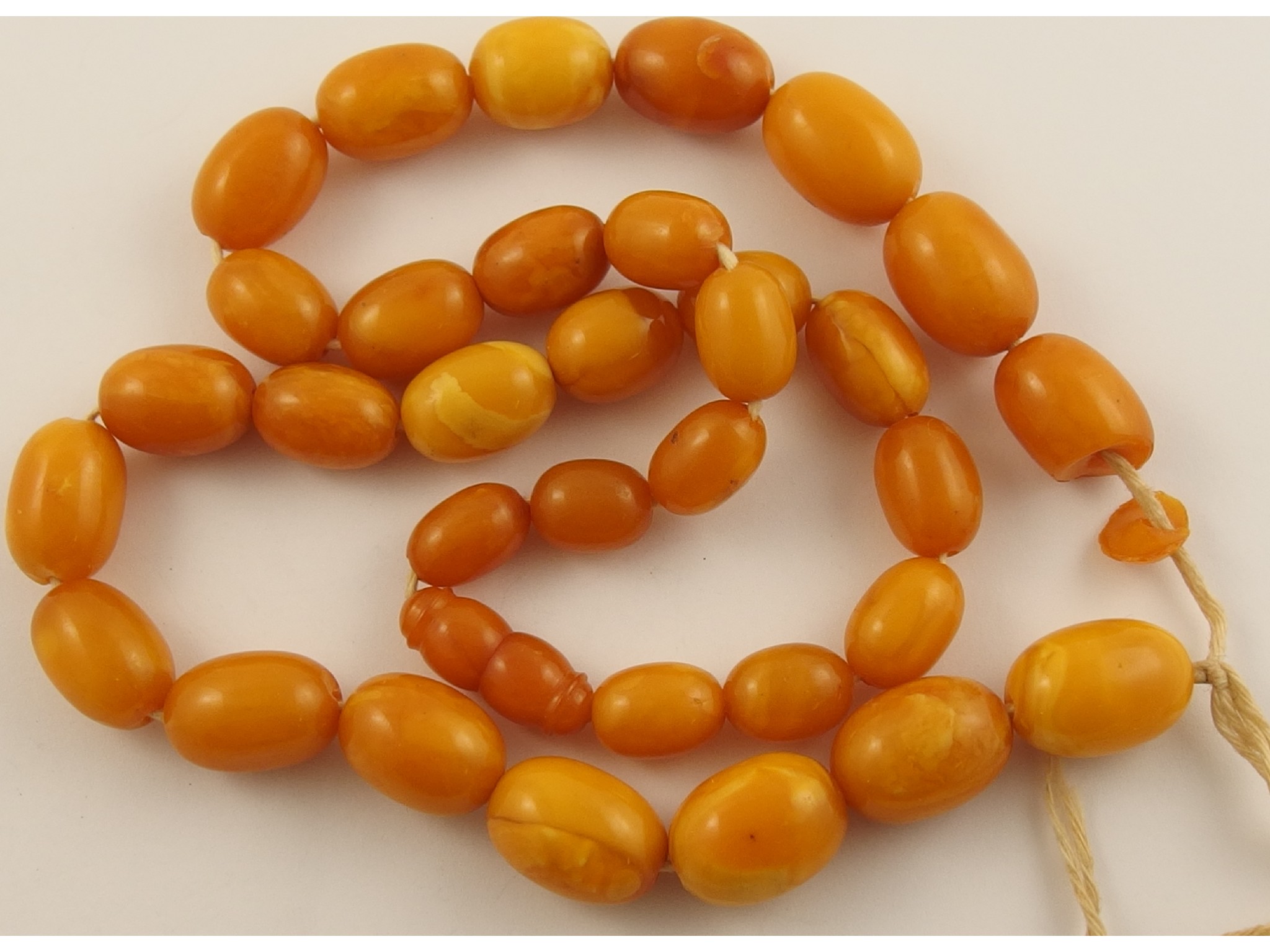 Appraisal: A string of yellow amber coloured beadsthe beads of swirled