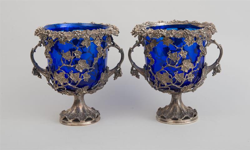 Appraisal: PAIR OF CONTINENTAL SILVERED METAL URNS With blue glass liners