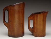 Appraisal: TWO CARVED WOOD PITCHERS Of different sized with similar cylindrical