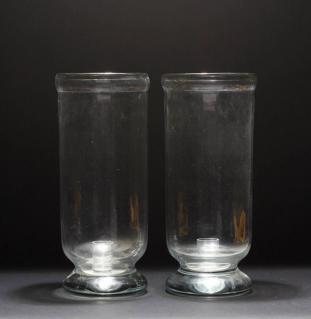 Appraisal: A PAIR OF CYLINDRICAL GLASS HURRICANE LAMPS with candle holders