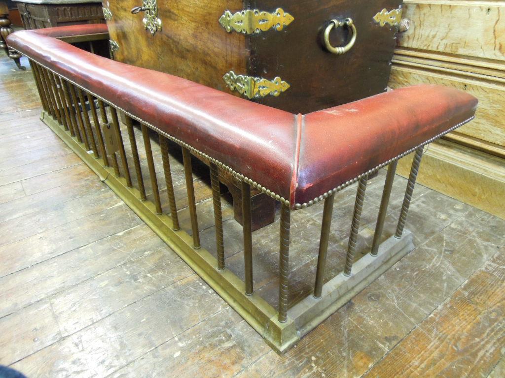 Appraisal: A large brass club fender with upholstered rail raised on