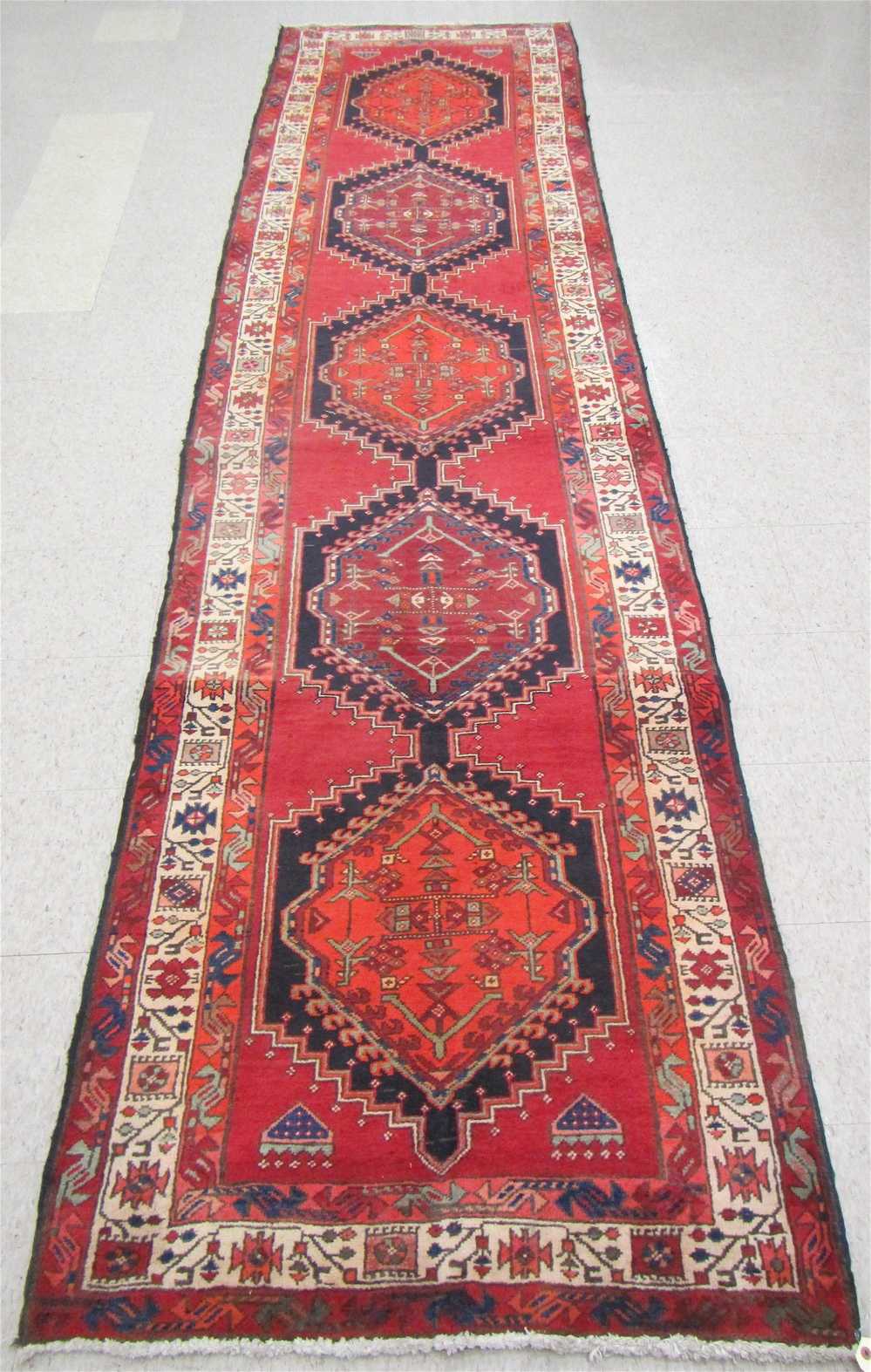 Appraisal: PERSIAN TRIBAL RUNNER repeating Kazak medallion design on red ground