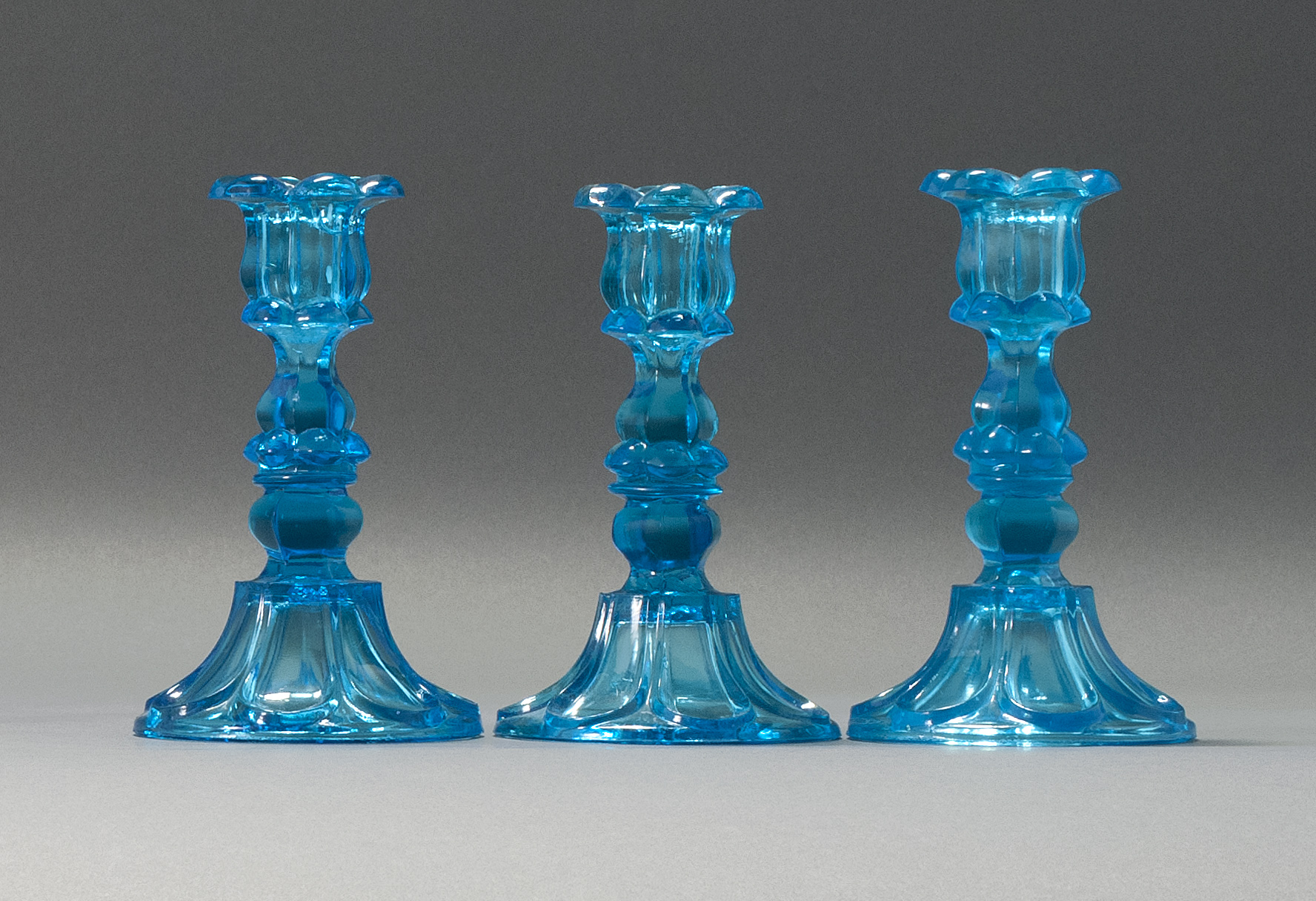 Appraisal: THREE SANDWICH GLASS COMPANY PRESSED GLASS CANDLESTICKS Mid- th CenturyIn