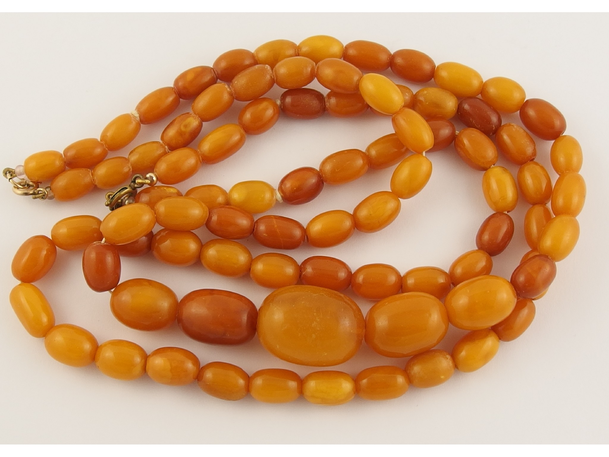 Appraisal: Two strings of amber coloured beadslarger beads biggest bead mm