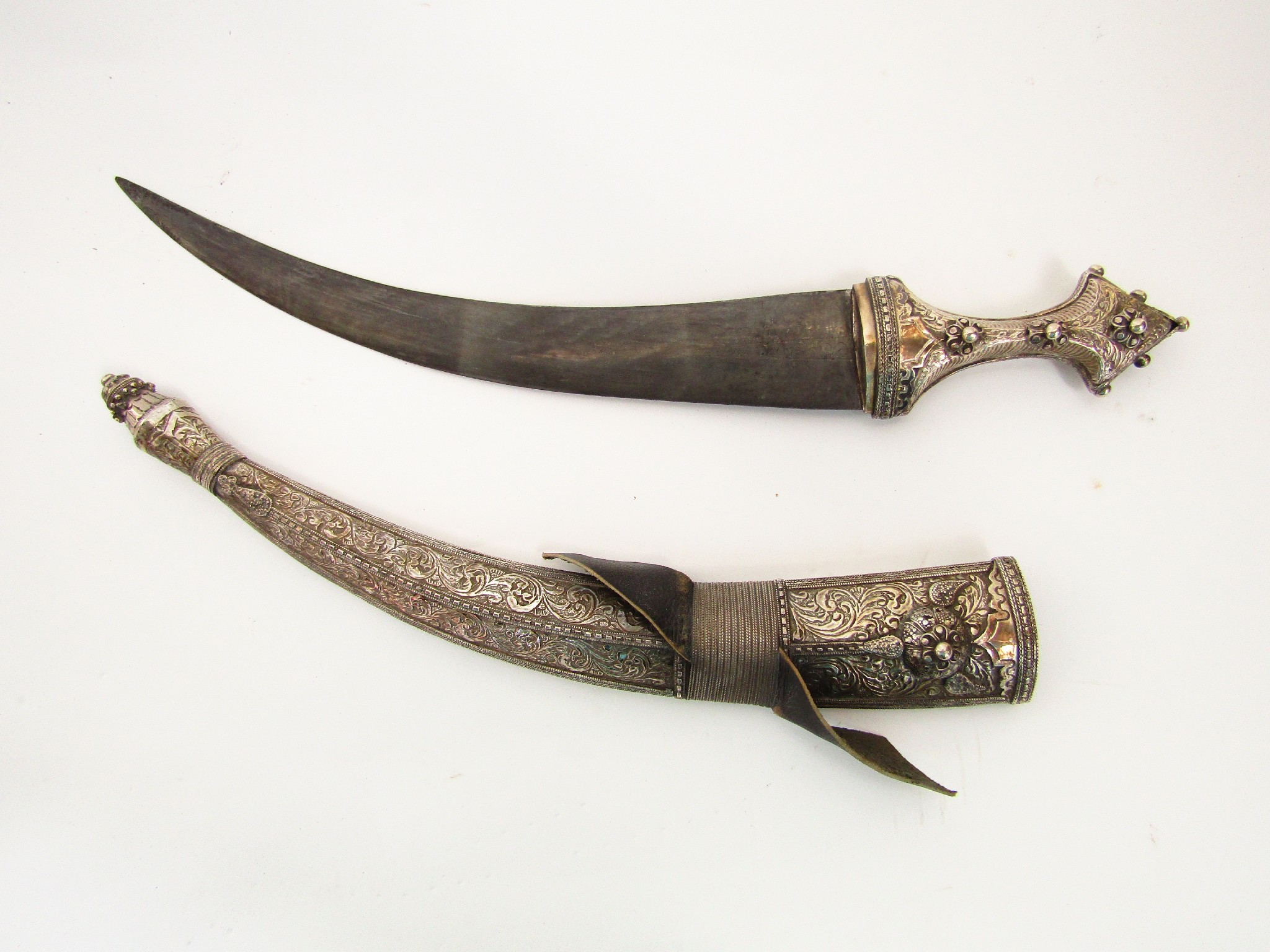 Appraisal: An Eastern curved dagger in heavily embossed white metal sheath