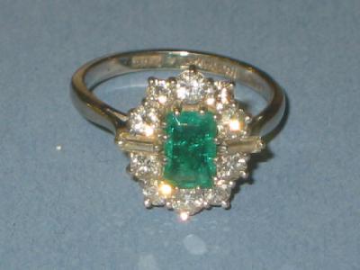 Appraisal: AN EMERALD AND DIAMOND CLUSTER RING comprising central trapp cut