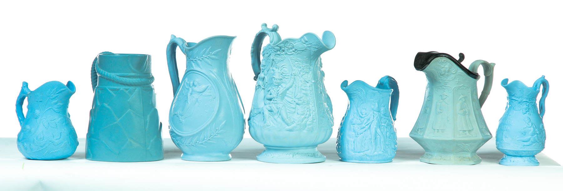 Appraisal: SEVEN RELIEF MOLDED SCENIC BLUE PITCHERS English Mid th century